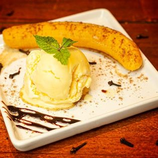BANANA FLAMBADA Banana cozida na calda preparada com suco de laranja com cravo e licores, servida com sorvete de creme, coberturas de morango, chocolate e canela em pó.